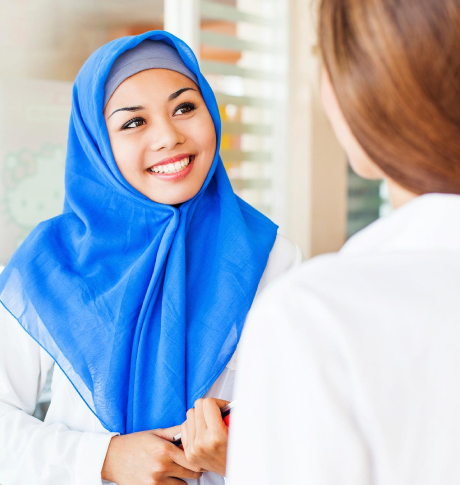 Muslim woman in blue headscarf smiling to another woman 